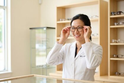 Opticienne indépendante souriante dans sa boutique d'optique moderne, ajustant une monture de lunettes derrière le comptoir